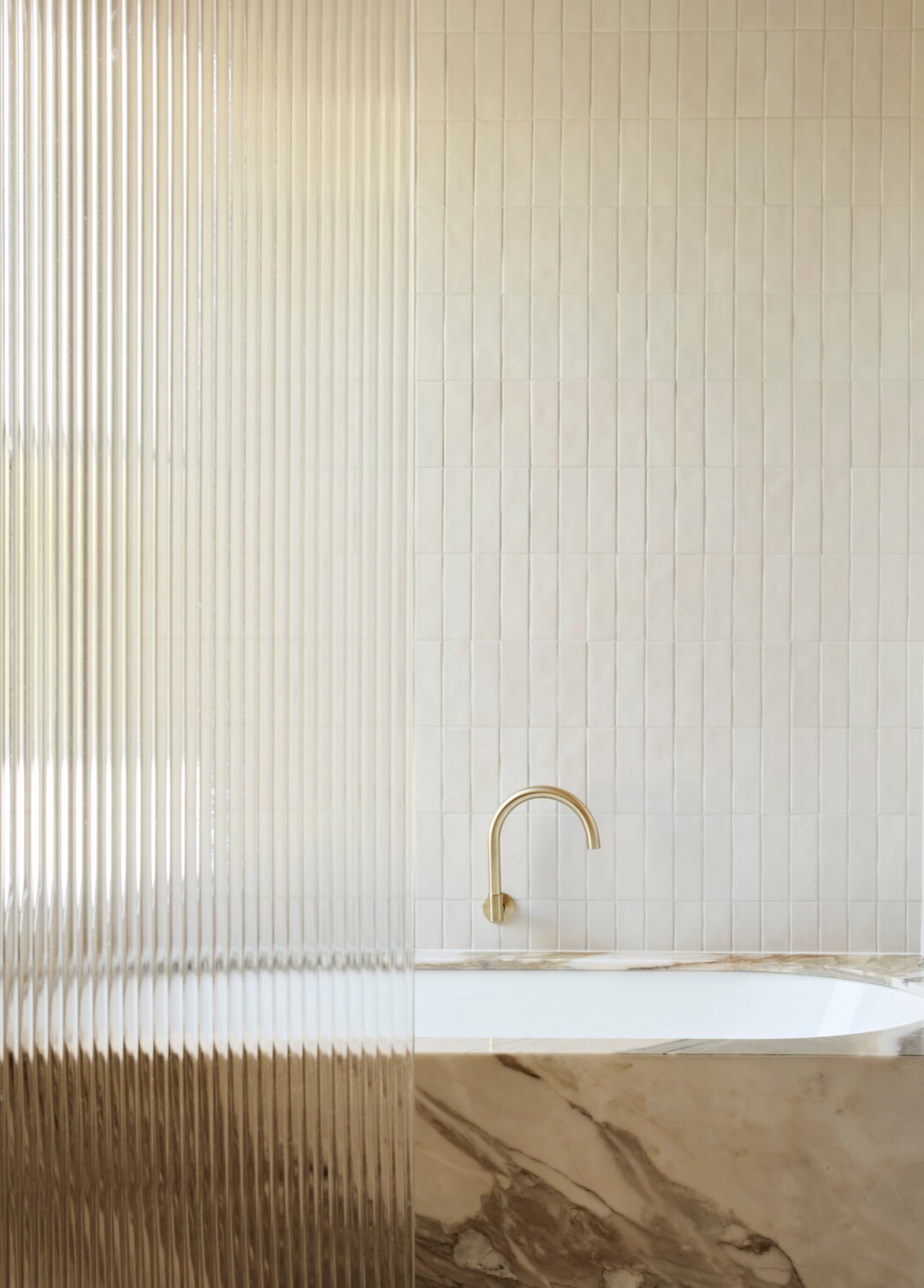 Interior design by Larritt-Evans — a fluted-glass bathroom with a marble bath and brass tapware.