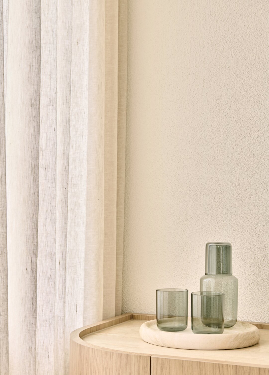 Interior styling by Larritt-Evans — green glassware on a tray beside a linen curtain.