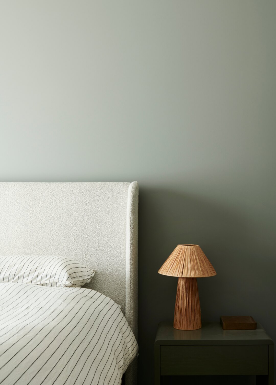 Interior design by Larritt-Evans — a calm bedroom with a sage headboard and rattan lamp.